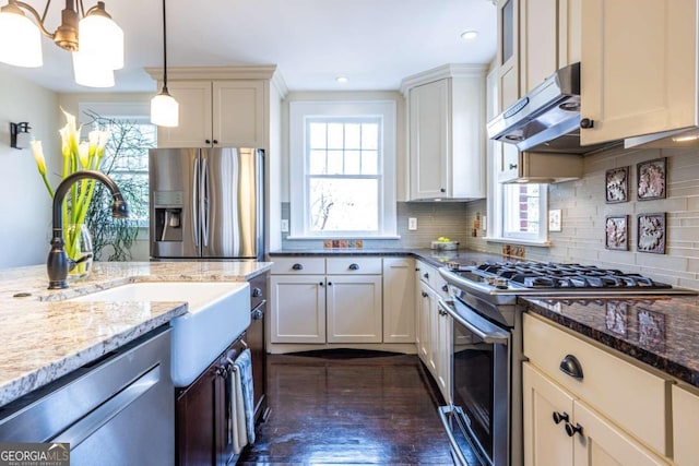 kitchen with light stone counters, decorative light fixtures, backsplash, appliances with stainless steel finishes, and under cabinet range hood