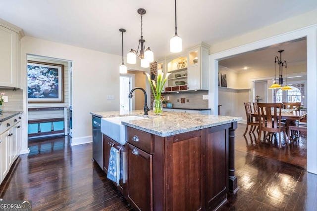 kitchen featuring an island with sink, glass insert cabinets, light stone counters, pendant lighting, and a sink