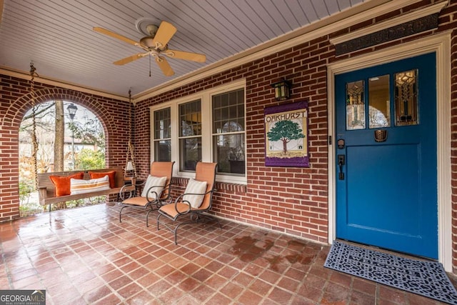 view of exterior entry featuring ceiling fan, a porch, and brick siding