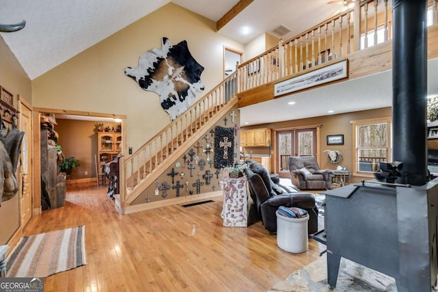 living room featuring stairs, high vaulted ceiling, light wood finished floors, and a wood stove