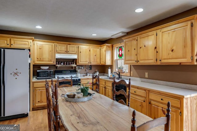 kitchen featuring light countertops, stainless steel microwave, freestanding refrigerator, gas range, and under cabinet range hood