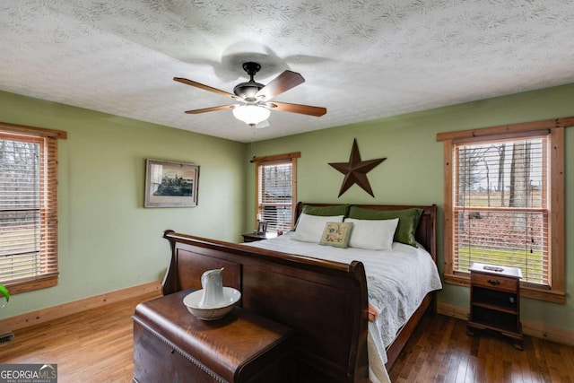 bedroom featuring visible vents, a textured ceiling, baseboards, and wood finished floors