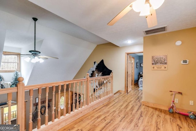 corridor with an upstairs landing, visible vents, vaulted ceiling, baseboards, and light wood-type flooring