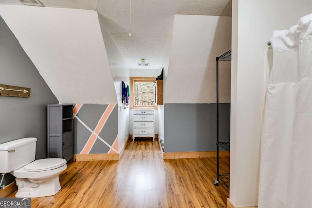 bathroom featuring toilet, a textured ceiling, vaulted ceiling, and wood finished floors