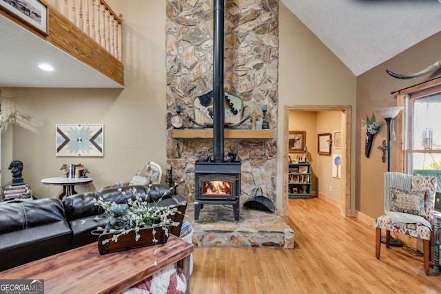 living room featuring high vaulted ceiling, a wood stove, light wood-style flooring, and baseboards