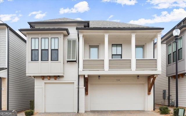 view of front facade featuring driveway, a balcony, roof with shingles, a garage, and brick siding