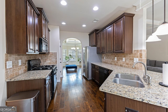 kitchen with arched walkways, light stone counters, a sink, black appliances, and decorative light fixtures