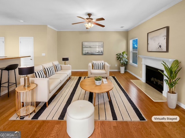 living area featuring ceiling fan, a high end fireplace, baseboards, light wood-type flooring, and crown molding