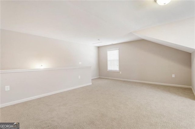 additional living space featuring light colored carpet, vaulted ceiling, and baseboards