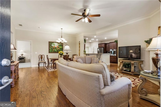 living room featuring ceiling fan with notable chandelier, dark wood-type flooring, visible vents, baseboards, and crown molding