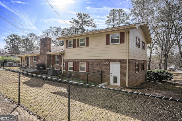 tri-level home with a fenced backyard, central AC unit, and brick siding