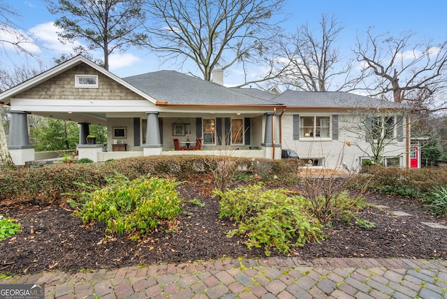 view of front of property featuring covered porch, a chimney, and a shingled roof