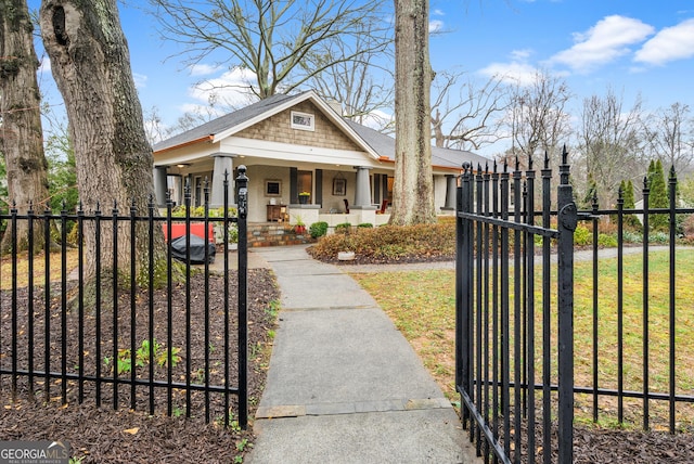 view of front of house featuring a fenced front yard, covered porch, a shingled roof, and a gate