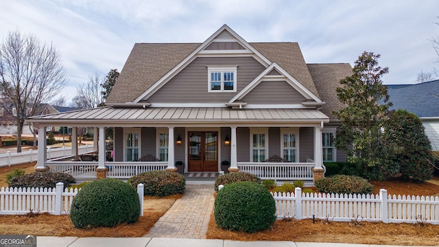 farmhouse inspired home featuring a fenced front yard, roof with shingles, a standing seam roof, french doors, and a porch