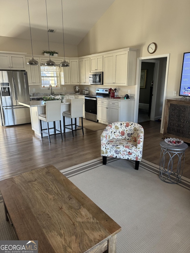 kitchen featuring stainless steel appliances, visible vents, a center island, a kitchen bar, and decorative light fixtures