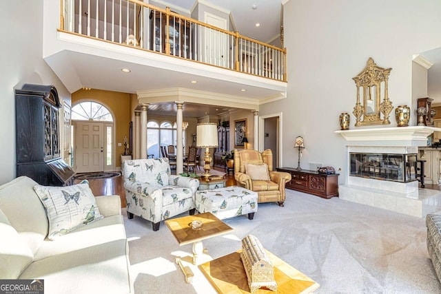 living room featuring decorative columns, a tiled fireplace, a high ceiling, and carpet flooring