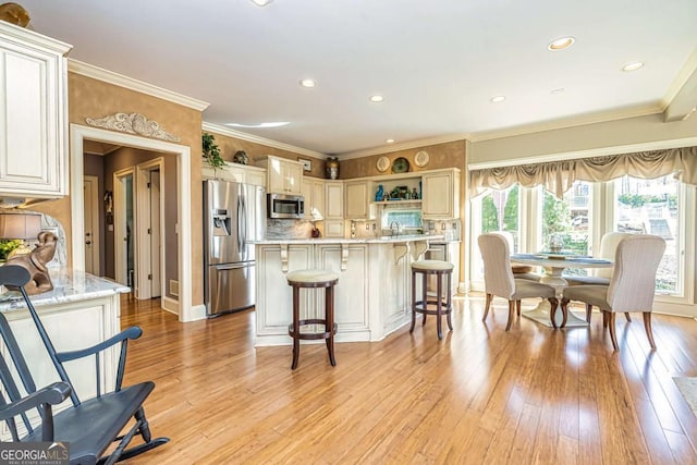 kitchen with appliances with stainless steel finishes, a kitchen breakfast bar, crown molding, light wood-style floors, and backsplash