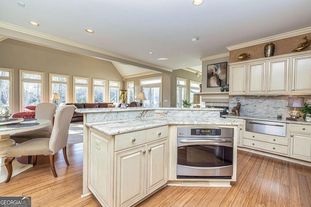 kitchen featuring a warming drawer, light wood finished floors, backsplash, stainless steel oven, and light stone countertops