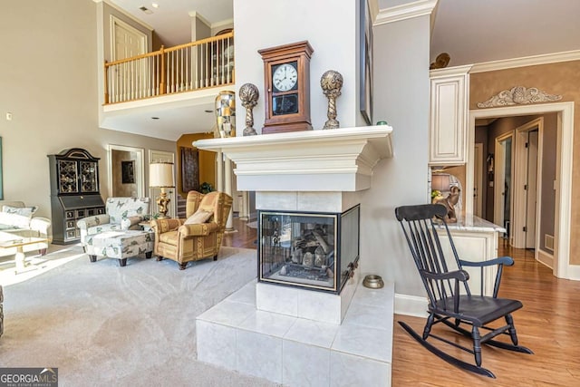 living area featuring a tile fireplace, a high ceiling, wood finished floors, baseboards, and ornamental molding