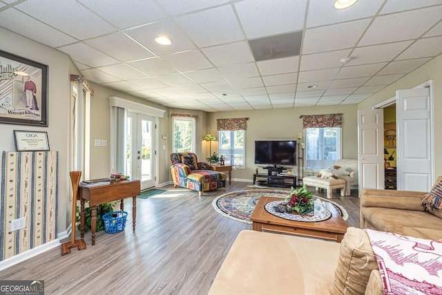 living area featuring french doors, a drop ceiling, baseboards, and wood finished floors