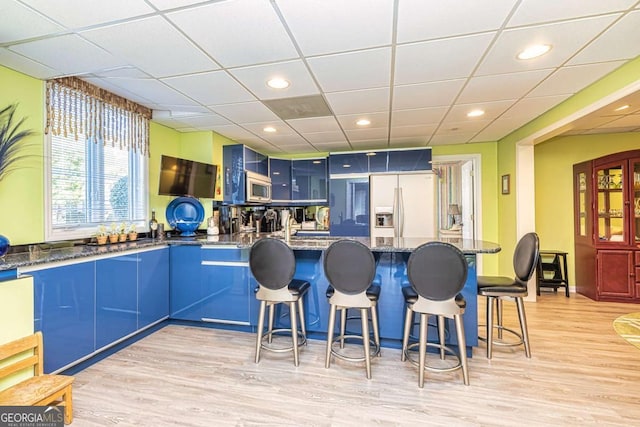 kitchen with a breakfast bar, stainless steel microwave, refrigerator with ice dispenser, and blue cabinets