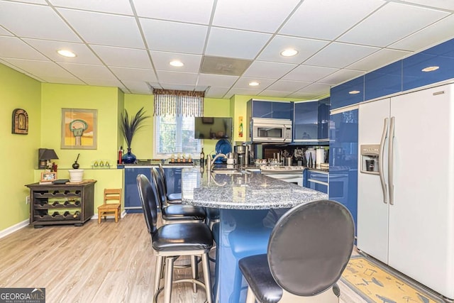 kitchen with blue cabinetry, white fridge with ice dispenser, stainless steel microwave, and a kitchen breakfast bar