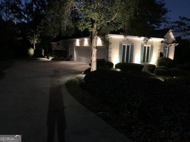 property exterior at night featuring a garage, driveway, and stucco siding