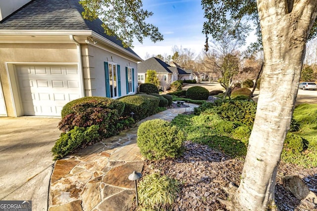 view of side of home featuring a shingled roof, driveway, a garage, and stucco siding