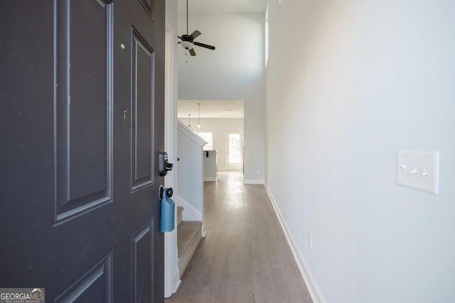 entrance foyer with ceiling fan, a towering ceiling, baseboards, light wood-style floors, and stairway