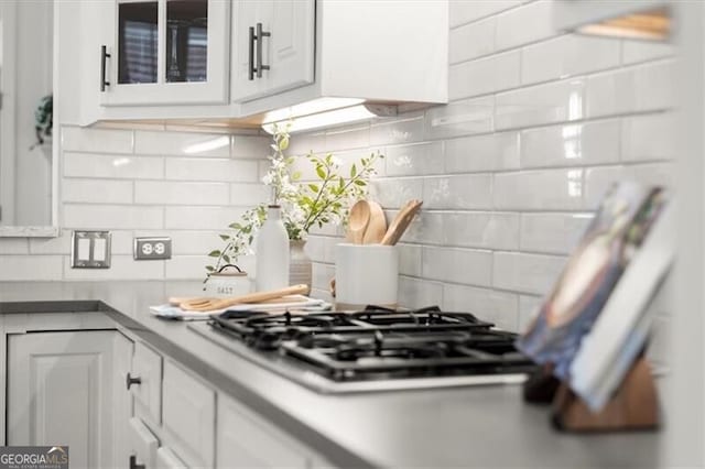 kitchen featuring glass insert cabinets, white cabinets, stainless steel gas stovetop, and decorative backsplash