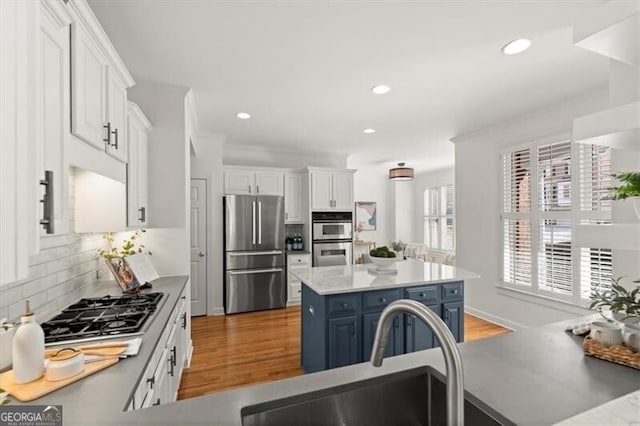 kitchen with stainless steel appliances, a kitchen island, white cabinetry, light countertops, and blue cabinetry