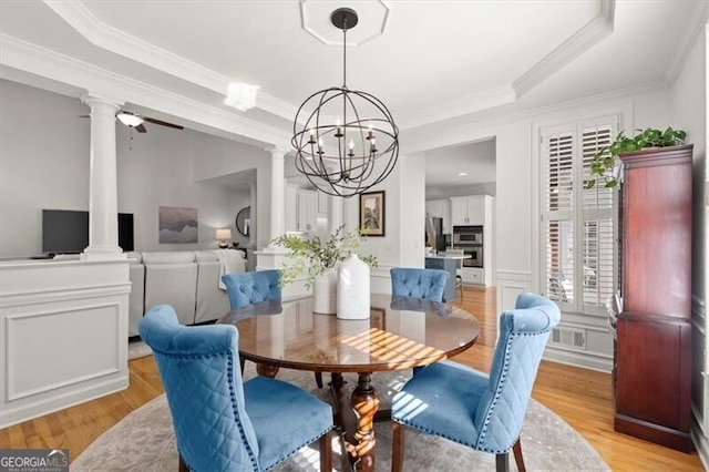 dining room featuring visible vents, a raised ceiling, light wood-style flooring, and ornate columns