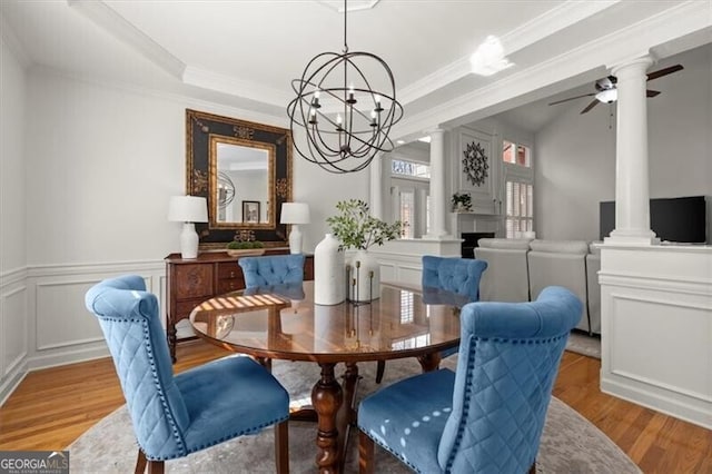 dining room with a decorative wall, ceiling fan with notable chandelier, ornamental molding, light wood-type flooring, and ornate columns