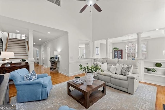 living room featuring decorative columns, baseboards, light wood-style flooring, a wealth of natural light, and ceiling fan with notable chandelier