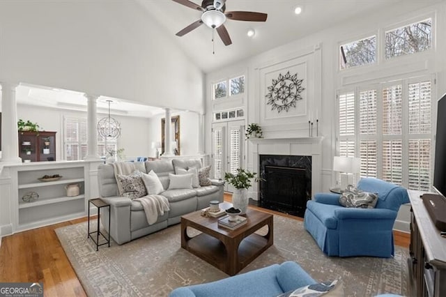 living area featuring high vaulted ceiling, plenty of natural light, decorative columns, and wood finished floors