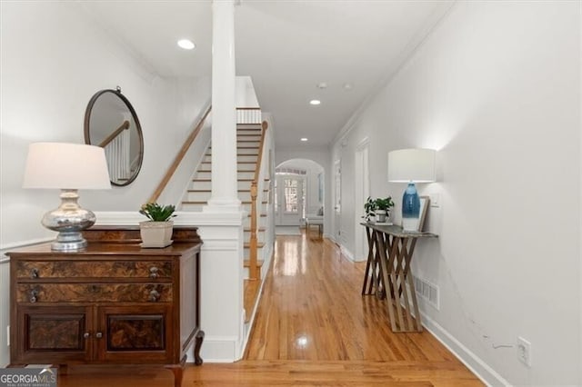 hall with light wood finished floors, stairs, arched walkways, and recessed lighting