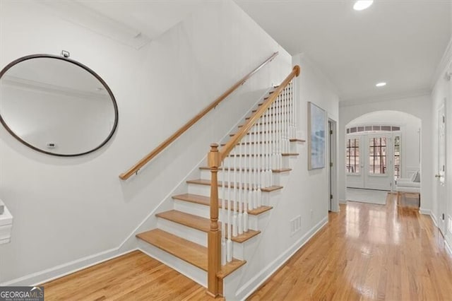 staircase featuring arched walkways, french doors, visible vents, and wood finished floors