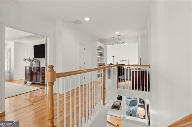 hallway with crown molding, visible vents, wood finished floors, and an upstairs landing