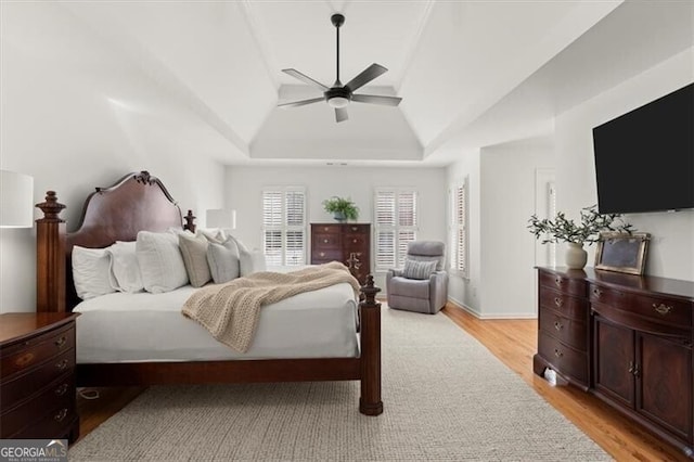 bedroom with light wood-style floors, ceiling fan, a tray ceiling, and baseboards