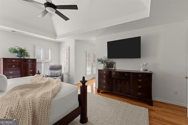 bedroom with lofted ceiling, ceiling fan, baseboards, light wood-type flooring, and a raised ceiling