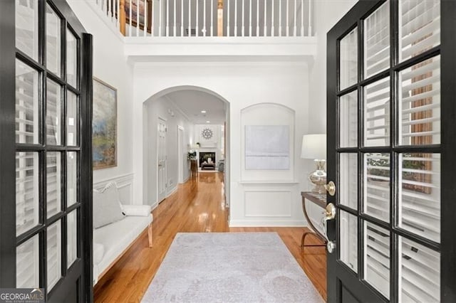 interior space with arched walkways, a towering ceiling, light wood-style flooring, and a decorative wall