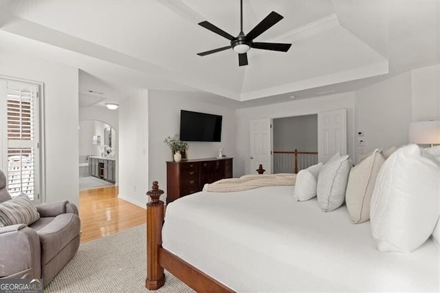 bedroom featuring light wood-style floors, a tray ceiling, arched walkways, and ensuite bath