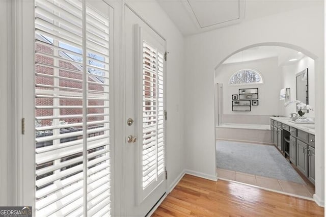 doorway to outside with arched walkways, light wood finished floors, a healthy amount of sunlight, and baseboards