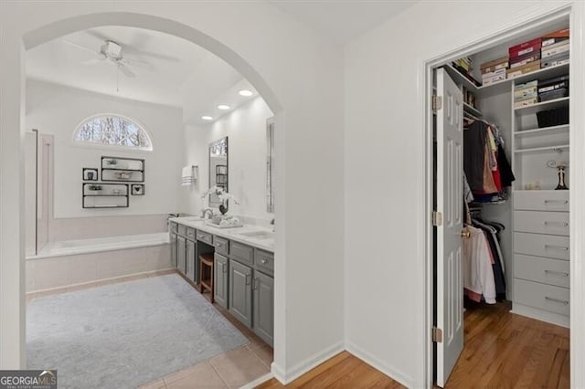 bathroom with wood finished floors, ceiling fan, vanity, and a bath