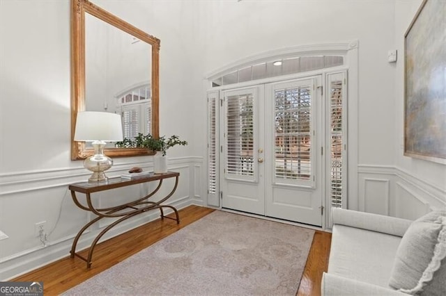 foyer entrance with french doors, a wainscoted wall, a decorative wall, and wood finished floors