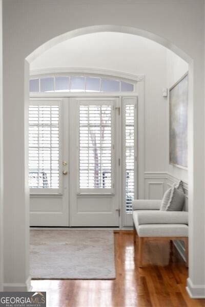 doorway to outside featuring french doors, a wainscoted wall, a decorative wall, and wood finished floors