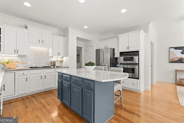 kitchen with appliances with stainless steel finishes, white cabinetry, a kitchen island, and light wood-style flooring