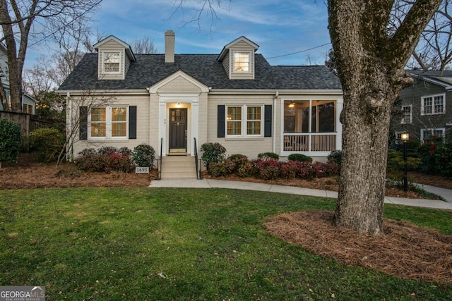 new england style home with a shingled roof, a front yard, and a chimney