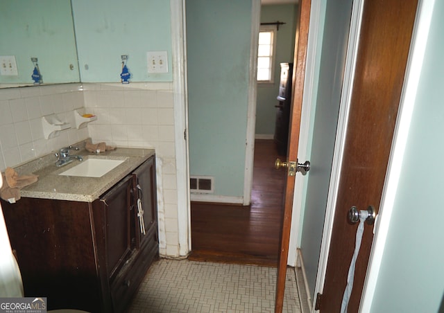 half bathroom with tile patterned floors, visible vents, tile walls, and vanity