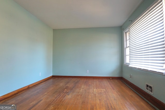 unfurnished room featuring wood finished floors, visible vents, and baseboards